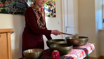 Eine Frau steht vor mehreren Klangschalen und schlägt gerade eine an.