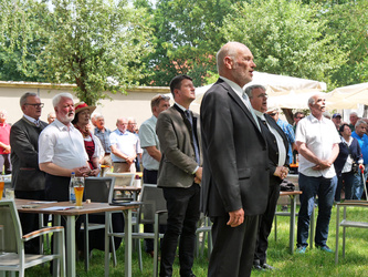 Blick von der Seite auf eine Gruppe stehender Menschen im Biergarten. Sie singen das Ave Maria.