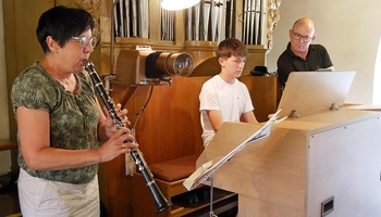 Von links nach rechts ist eine Frau mit Klarinette, ein Jugendlicher an der Orgel und ein Mann im Hintergrund zu sehen.