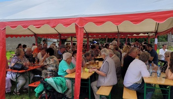 Blick auf Bierbänke und -tische an denen viele Menschen mit einem Glas Bier sitzen.