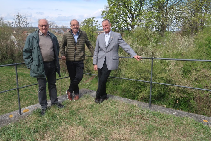 Drei Männer lehnen an ein Geländer und schauen freundlich in die Kamera.