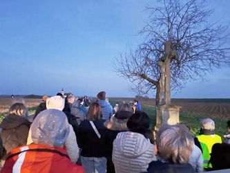 Eine Gruppe Menschen ist von hinten zu sehen. Fotografiert ist das Wegkreuz.