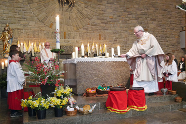 Vor dem Altar in der Dipbacher Kirche stehen Osterspeisen. Der Pfarrer besprengt sie mit Weihwasser.