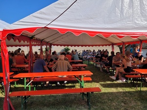 Menschen sitzen in einem Festzelt an Bierbänken.