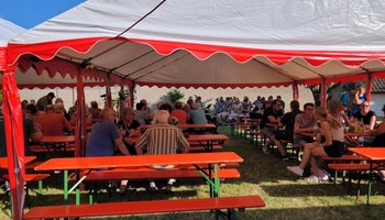 Menschen sitzen in einem Festzelt an Bierbänken.