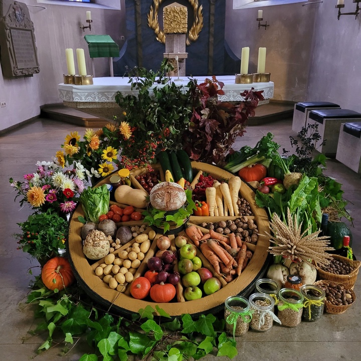 vor dem Altar liegt ein altes Wagenrad, innerhalb und außerhalb liegen verschiedene Sorten Gemüse, Nüsse, Getreide und Blumen schön angeordnet