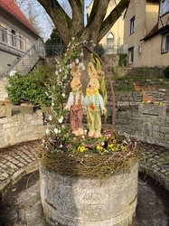 Auf einem runden Steinbrunnen sitzen zwei bunte Deko-Osterhasen.