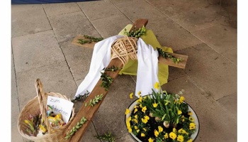 Ein liegendes Kreuz, das mit grünen Zweigen und Blumen dekoriert ist, als Symbol für den Ostersonntag.