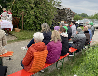 Auf einigen Bierbänken sitzen Menschen. Sie haben Jacken an und schauen alle in die gleiche Richtung nach links.