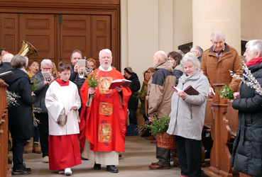 Eine Gruppe an Menschen und einige Musikanten ziehen durch den Mittelgang der Wallfahrtkirche. Der Pfarrer hat ein rotes Messgewand an und geht voran.