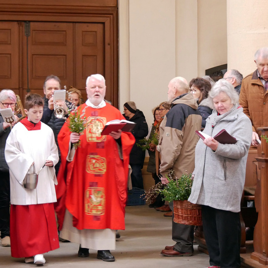 Eine Gruppe an Menschen und einige Musikanten ziehen durch den Mittelgang der Wallfahrtkirche. Der Pfarrer hat ein rotes Messgewand an und geht voran.