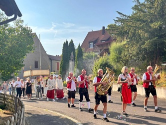 Blick auf die Dorfstraße. Man sieht die Musikkapelle beim Spielen und dahinter den Altardienst.