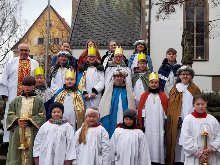 Ein Gruppenbild von den Sternsingern mit dem Diakon auf der Treppe vor der Kirche in Dipbach.