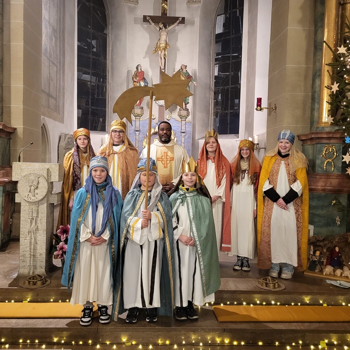 Acht Sternsinger und Kaplan Dunstan stehen im Altarraum der Kirche und schauen in die Kamera