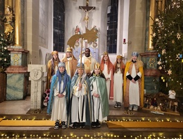 Acht Sternsinger und Kaplan Dunstan stehen im Altarraum der Kirche und schauen in die Kamera