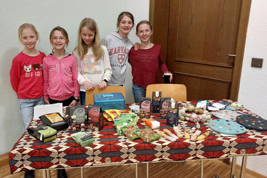 Fünf Kinder stehen hinter einem Tisch und freuen sich.