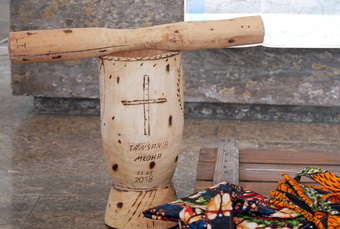 Afrikanische Gegenstände aus Holz und Stoff sind auf dem Boden trappiert. Auf einem Holzstück steht das Wort Mkoha und das Datum.