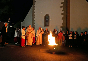 Ein Osterfeuer brennt auf dem Kirchplatz in Dipbach. Die Menschen, die dahinter stehen, sind vom Feuerschein erhellt.