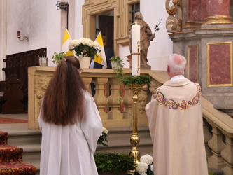 Eine Ministrantin und Pater Matthäus stehen vor der neuen Osterkerze.