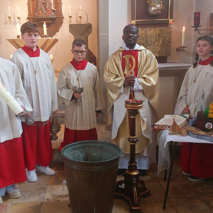Father Benjamin und vier Ministranten in der Kirche in Püssensheim schauen zum Fotografen. Sie haben die Osterkerze dabei.