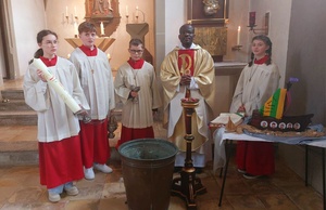 Father Benjamin und vier Ministranten in der Kirche in Püssensheim schauen zum Fotografen. Sie haben die Osterkerze dabei.