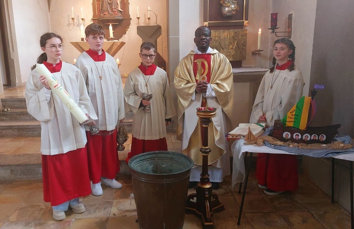 Father Benjamin und vier Ministranten in der Kirche in Püssensheim schauen zum Fotografen. Sie haben die Osterkerze dabei.