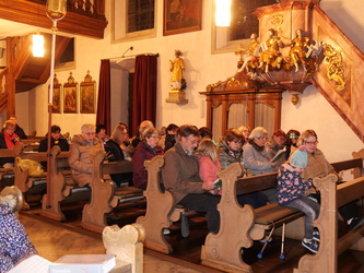 Blick von vorn in den Kirchenraum. In den Bänken sitzen Menschen.