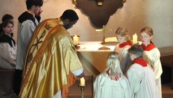 Kaplan Louis Odidi und die neuen Ministrant:innen entzünden gemeinsam eine Kerze.