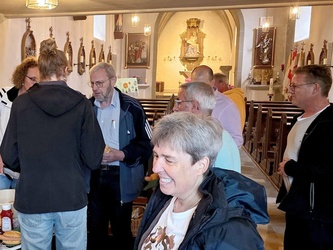 In der Kirche sitzen und stehen Menschen. Sie essen etwas und unterhalten sich.