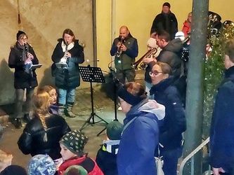 Im hinteren Teil des Bildes stehen drei Musikanten und spielen ein Instrument. Davor sieht man Menschen mit Martinslaternen.