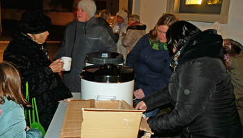 Auf dem Kirchplatz stehen Menschen um einen großen Topf mit Glühwein.