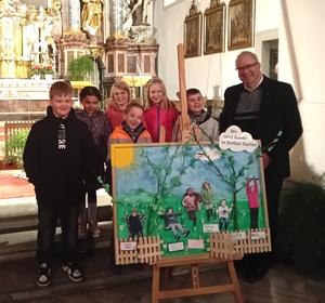 Die Kommunionkinder stehen zusammen mit dem Pfarrer hinter einem großen Bild, welches einen Garten zeigt und welches die persönlichen Vorstellungen der Kinder enthält.