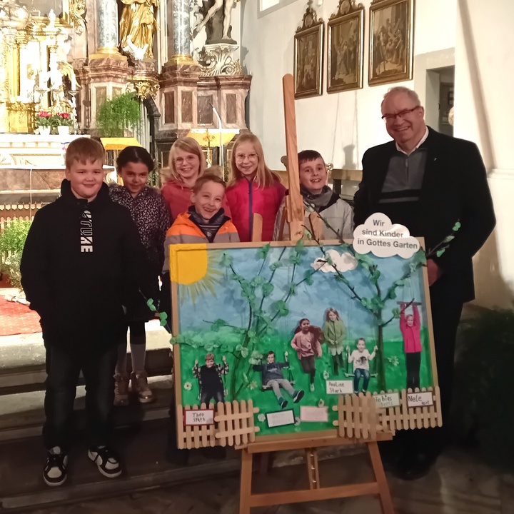 Die Kommunionkinder stehen zusammen mit dem Pfarrer hinter einem großen Bild, welches einen Garten zeigt und welches die persönlichen Vorstellungen der Kinder enthält.