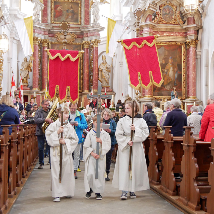 Ministranten mit dem Kreuz und zwei Fahnen ziehen aus der Kirche aus.