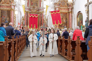 Ministranten mit dem Kreuz und zwei Fahnen ziehen aus der Kirche aus.