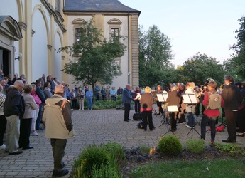 Am Seitenausgang der Wallfahrtskirche spielt rechts die Musikkapelle. Um sie herum stehen Menschen und hören zu.