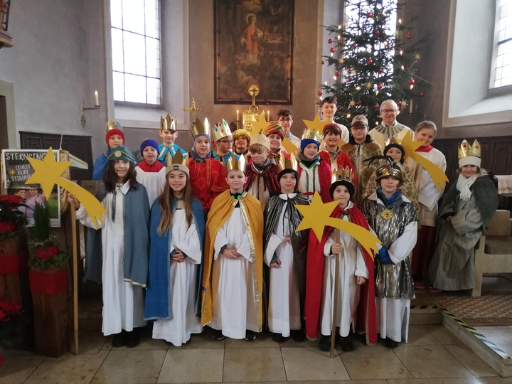 Die 22-köpfige Sternsingergruppe steht auf den Altarstufen in der Kirche. Alle schauen in die Kamera.