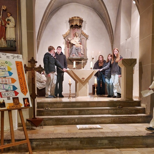 Sechs Jugendliche stehen um den Altar in der Püssensheimer Kirche. Links ist ihr Firmplakat zu sehen.