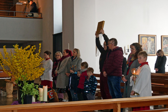 Eine Gruppe Kinder und Erwachsene blicken in eine Richtung. In der Mitte wird ein Messbuch hochgehoben.