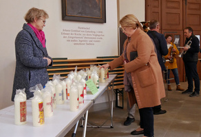 Auf einem Tisch stehen mehrere Osterkerzen. Links vom Tisch ist Frau Altenhöfer. Rechts vom Tisch steht eine Frau und schaut sich die Kerzen an.