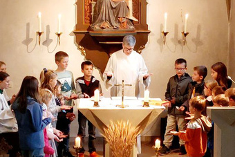 Am Altar der Kirche in Püssensheim steht die Gemeindereferentin. Um sie herum sind mehrere Kinder.