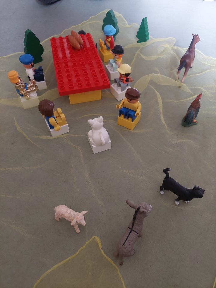 Lego-Figuren sitzen um einen Tisch. Um sie herum sind mehrere Tiere