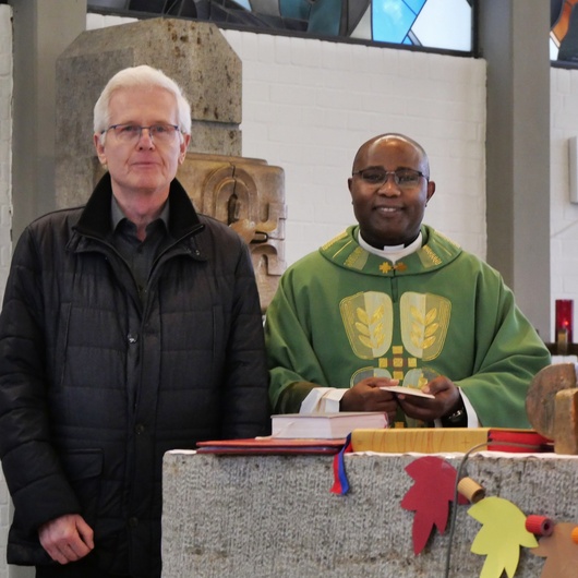 Zwei Männer stehen nebeneinander hinter dem Altar der Kirche und schauen freundlich in die Kamera.