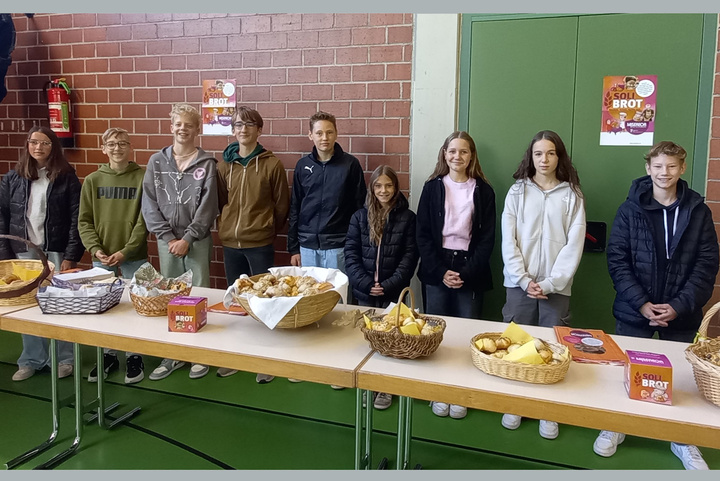 Hinter einem Tisch stehen in einer Reihe mehrere Jugendliche.