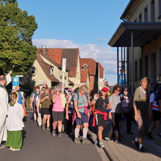Die Kreuzbergwallfahrenden auf den Stufen zur Kirche in Bergheim. Pastoralreferent Meier besprengt sie mit Weihwasser.
