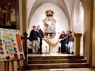 Sechs Jugendliche stehen um den Altar in der Kirche in Püssensheim. Vorne links ist ihr Firmplakat zu sehen.