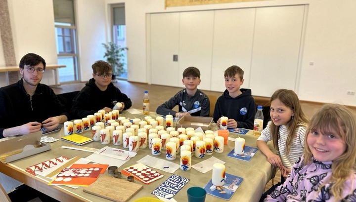 Eine Gruppe an Kindern und Jugendlichen sitzen um einen Tisch. Darauf stehen verzierte Kerzen.