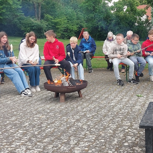 Um eine Feuerstelle sitzen ein paar Jugendliche beim Grillen