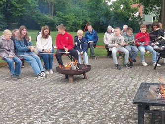 Um eine Feuerstelle sitzen ein paar Jugendliche beim Grillen
