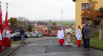 Der Pfarrer, Ministranten und mehrere Menschen stehen neben dem Bildstock in der Bergstraße.